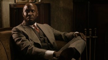 Movie still from “Bessie” (2015), directed by Dee Rees – A man sitting on a couch wearing a suit and tie; Medium shot, Low angle