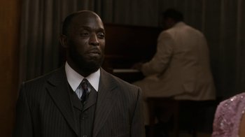 Movie still from “Bessie” (2015), directed by Dee Rees – A man in a suit and tie standing in front of a piano; Close Up shot, Over the shoulder angle