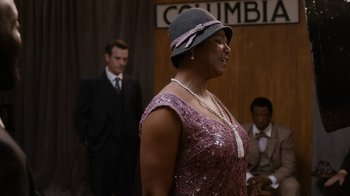 Movie still from “Bessie” (2015), directed by Dee Rees – A woman in a purple dress and a gray hat; Medium shot, Over the shoulder angle