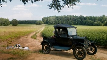 Movie still from “Bessie” (2015), directed by Dee Rees – An old car is parked on the side of a dirt road; Extreme Wide shot, High angle