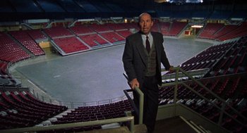 Movie still from “Best in Show” (2000), directed by Christopher Guest – A man in a suit and tie standing in an empty stadium; Wide shot, High angle
