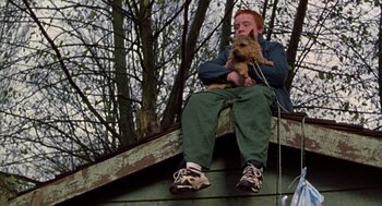 Movie still from “Best in Show” (2000), directed by Christopher Guest – A man sitting on top of a roof holding a dog; Medium shot, Low angle