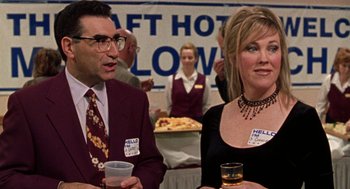 Movie still from “Best in Show” (2000), directed by Christopher Guest – A man and a woman are standing next to each other holding drinks; Medium shot, Over the shoulder angle