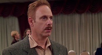 Movie still from “Best in Show” (2000), directed by Christopher Guest – A person wearing a suit and tie; Close Up shot, Over the shoulder angle