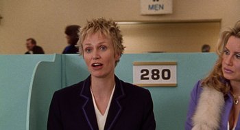 Movie still from “Best in Show” (2000), directed by Christopher Guest – A woman with blonde hair is standing in a room; Medium shot, Over the shoulder angle