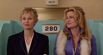 Movie still from “Best in Show” (2000), directed by Christopher Guest – Two women are standing next to each other in front of a sign; Medium shot, Low angle