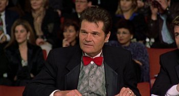 Movie still from “Best in Show” (2000), directed by Christopher Guest – A man with a red bow tie sitting in front of a group of people; Close Up shot, Low angle