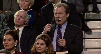 Movie still from “Best in Show” (2000), directed by Christopher Guest – A man in a suit and tie holding a spoon in his mouth; Medium shot, Over the shoulder angle