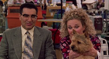 Movie still from “Best in Show” (2000), directed by Christopher Guest – A man and a woman sitting next to each other with a dog; Medium shot, Over the shoulder angle