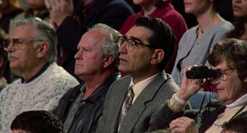 Movie still from “Best in Show” (2000), directed by Christopher Guest – A man wearing glasses and a suit is sitting in a crowd; Close Up shot, High angle