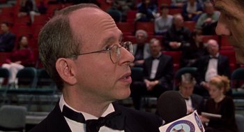 Movie still from “Best in Show” (2000), directed by Christopher Guest – A man in a tuxedo is talking into a microphone in front of an audience; Close Up shot, High angle