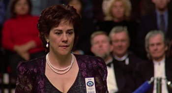Movie still from “Best in Show” (2000), directed by Christopher Guest – A woman in a crowd of people wearing pearls and a purple dress; Close Up shot, Over the shoulder angle