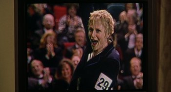 Movie still from “Best in Show” (2000), directed by Christopher Guest – A woman with blonde hair is smiling in front of an audience; Close Up shot, Low angle