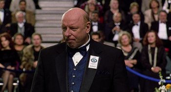 Movie still from “Best in Show” (2000), directed by Christopher Guest – A man in a suit and tie standing in front of a crowd of onlookers; Close Up shot, Over the shoulder angle