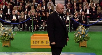 Movie still from “Best in Show” (2000), directed by Christopher Guest – A man standing in front of a crowd of people; Wide shot, Over the shoulder angle
