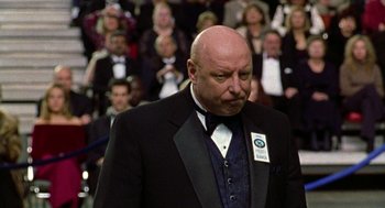Movie still from “Best in Show” (2000), directed by Christopher Guest – A man in a suit and tie standing in front of an audience; Close Up shot, Over the shoulder angle