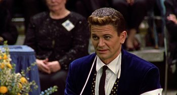 Movie still from “Best in Show” (2000), directed by Christopher Guest – A man in a suit and tie sitting in front of a crowd; Close Up shot, Over the shoulder angle