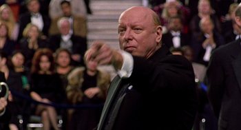 Movie still from “Best in Show” (2000), directed by Christopher Guest – An older man in a black suit and white shirt is holding his arm out; Close Up shot, Low angle