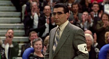 Movie still from “Best in Show” (2000), directed by Christopher Guest – A man in a suit and tie standing in front of a group of people; Close Up shot, Low angle