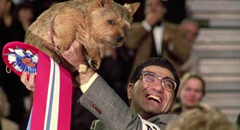 Movie still from “Best in Show” (2000), directed by Christopher Guest – A man holding a dog up in the air; Medium shot, Low angle