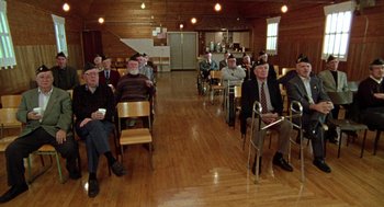 Movie still from “Best in Show” (2000), directed by Christopher Guest – A group of men sitting in chairs in a room; Wide shot, High angle