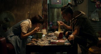Two people sitting at a table eating noodles