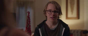 Movie still from “Better Watch Out” (2016), directed by Chris Peckover – A young man wearing glasses sitting in front of a christmas tree; Close Up shot, Over the shoulder angle