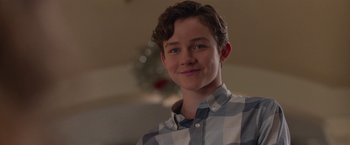Movie still from “Better Watch Out” (2016), directed by Chris Peckover – A young man smiling for the camera in front of a christmas tree; Close Up shot, Over the shoulder angle