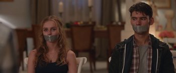 Movie still from “Better Watch Out” (2016), directed by Chris Peckover – Two people sitting at a dinner table with their mouths taped shut; Close Up shot, Over the shoulder angle