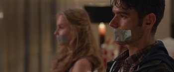Movie still from “Better Watch Out” (2016), directed by Chris Peckover – A man and a woman with their mouths taped shut; Close Up shot, Over the shoulder angle