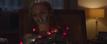 Movie still from “Better Watch Out” (2016), directed by Chris Peckover – A woman with a taped mouth and a string of lights around her neck; Close Up shot, Low angle