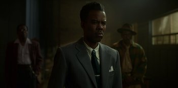 Movie still from “Fargo” (2014), created by Noah Hawley – A man in a suit and tie standing in a dimly lit room; Medium shot, Over the shoulder angle