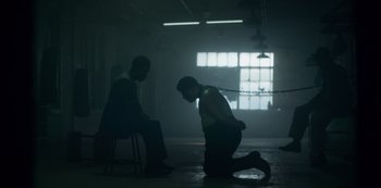 Movie still from “Fargo” (2014), created by Noah Hawley – A man kneeling on the ground with a chain around his neck; Wide shot, Low angle