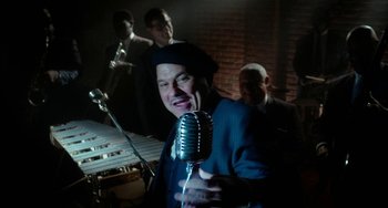 Movie still from “Big Eyes” (2014), directed by Tim Burton – A man holding a microphone in front of other men; Medium shot, High angle