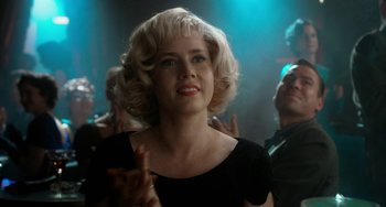 Movie still from “Big Eyes” (2014), directed by Tim Burton – A woman with blonde hair and red lipstick in front of a group of people; Close Up shot, Over the shoulder angle