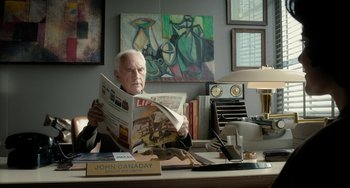 Movie still from “Big Eyes” (2014), directed by Tim Burton – An older man sitting at a desk reading a newspaper; Medium shot, High angle