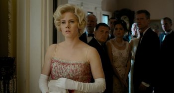 Movie still from “Big Eyes” (2014), directed by Tim Burton – A group of people standing in a room with a woman in a dress; Medium shot, Over the shoulder angle