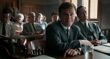 Movie still from “Big Eyes” (2014), directed by Tim Burton – A man sitting at a table in front of a group of people; Medium shot, Low angle