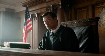 Movie still from “Big Eyes” (2014), directed by Tim Burton – A man sitting in front of an american flag in a courtroom; Medium shot, Low angle