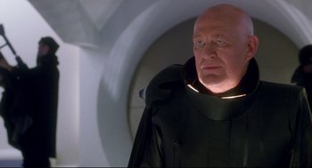 Movie still from “Bill & Ted's Bogus Journey” (1991), directed by Peter Hewitt – An older man wearing a black suit with a glowing light around his neck; Close Up shot, Low angle