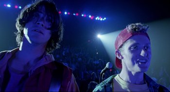 Movie still from “Bill & Ted's Bogus Journey” (1991), directed by Peter Hewitt – Two men are standing in front of a microphone in front of an audience; Medium shot, Low angle