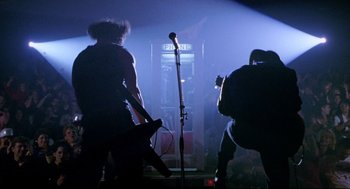 Movie still from “Bill & Ted's Bogus Journey” (1991), directed by Peter Hewitt – A man standing on a stage holding a microphone; Wide shot, Low angle