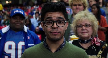 Movie still from “Billy Lynn's Long Halftime Walk” (2016), directed by Ang Lee – A person wearing glasses with people in the background; Close Up shot, Over the shoulder angle