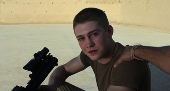 Movie still from “Billy Lynn's Long Halftime Walk” (2016), directed by Ang Lee – A young man sitting on the ground holding a rifle; Close Up shot, High angle