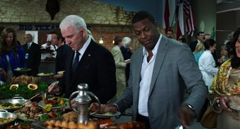 Movie still from “Billy Lynn's Long Halftime Walk” (2016), directed by Ang Lee – Two men standing at a buffet table with plates of food on it; Medium shot, Over the shoulder angle