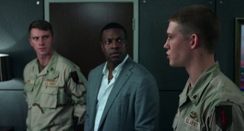 Movie still from “Billy Lynn's Long Halftime Walk” (2016), directed by Ang Lee – A man in a gray suit standing next to two other men; Medium shot, Over the shoulder angle