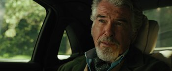 Movie still from “Black Adam” (2022), directed by Jaume Collet-Serra – An older man sitting in the back seat of a car; Close Up shot, Over the shoulder angle