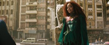 Movie still from “Black Adam” (2022), directed by Jaume Collet-Serra – A woman with red hair standing in front of a building; Medium shot, Over the shoulder angle