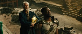 Movie still from “Black Adam” (2022), directed by Jaume Collet-Serra – A man standing next to another man wearing a helmet; Medium shot, Over the shoulder angle