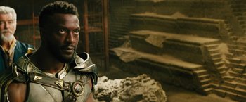 Movie still from “Black Adam” (2022), directed by Jaume Collet-Serra – A man in a costume standing in front of a stone wall; Close Up shot, Over the shoulder angle